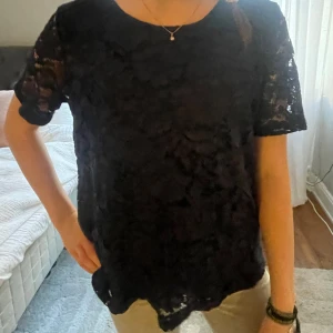 Mörkblå spetsblus - Säljer en elegant mörkblå spetsblus i mycket bra skick. Blusen har korta ärmar och ett vackert blommigt mönster. Perfekt för både fest och vardag. Storlek M med modellen är XS och den passar runt XS-M