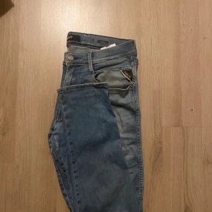 Blå jeans från Replay - Säljer ett par snygga blå jeans från Replay, modell hyperflex Anbass. De har en cool slitning på vänster ben och klassisk femficksdesign. Perfekta för en avslappnad stil och passar till både vardag och fest. Sköna och stilrena! Väldigt bra skick 