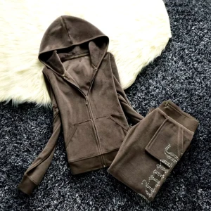 DupeSet från Juicy Couture - Säljer en supermjuk brun velour tracksuit som liknar originalet från Juicy Couture. Hoodien har dragkedja, en luva och detaljer bak på ryggen, medan byxorna har snygga strassdetaljer längs benet och praktiska fickor. Perfekt för en chill dag eller en avslappnad utflykt. Storlek M men känns som XS- S. Y2K set.