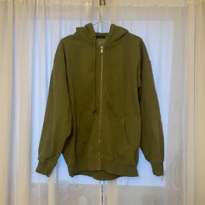 Olivgrön hoodie från Brandy Melville - Säljer en supermysig olivgrön hoodie från Brandy Melville. Den har en dragkedja framtill och en stor luva. Perfekt för höst och vår, och den är i bra skick med en liten defekt man ser på bild 3. Säljer för att den inte kommit till användning på över två år. Har två olika färger uppe!