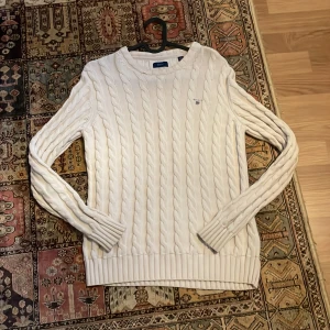 Vit stickad tröja från Gant - Säljer en stilren vit stickad tröja från Gant. Den har ett klassiskt flätmönster och är i mycket bra skick. Perfekt för höst och vinter, med långa ärmar och ribbade muddar. Passar både till vardags och lite finare tillfällen. Supermysig och varm!