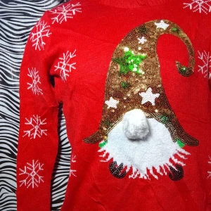 Röd jultröja med paljetter - Säljer en supermysig röd jultröja med en glittrig tomteluva i paljetter och snöflingor över hela tröjan. Perfekt för julfesten eller mysiga vinterdagar. Tröjan har långa ärmar och är i bra skick. 🎅✨