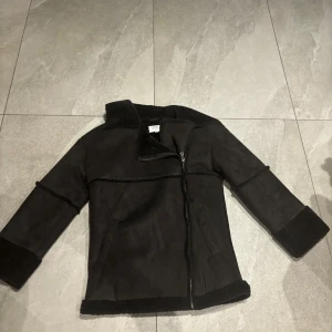 Svart jacka från Karo Kauer - Säljer en snygg svart jacka från Karo Kauer. Den har en dragkedja framtill och är gjord i ett mjukt material som ser ut som mocka. Jackan har långa ärmar och en stilren design som passar perfekt för höst och vinter. Perfekt för att hålla sig varm och trendig!