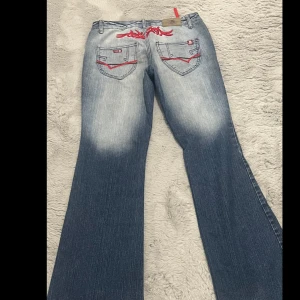 Vintage lågmidjade jeans  - Vintage låg midjade jeans med unik röd tryck där bak. Midjemått:82cm Innerbenslängd: 81cm ytterbens: 101cm Ganska svårt att hitta exakt samma! Us storlek: w28/29 fast passar w27 också! svensk storlek: 38/40 fast passar 36 också! PRISET KAN DISKUTERAS