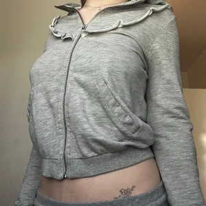 Grå zip-up  - Grå mysig kort zip-up med volang liknande detalj på. 