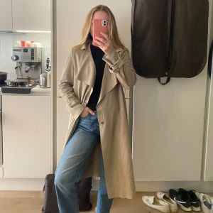 Beige trenchcoat med guldiga detaljer i mockaimitation  - Beige trenchcoat med guldiga detaljer i mockaimitation. Så fin, använd en gång. Som ny! Köpt för 1299 kr. 