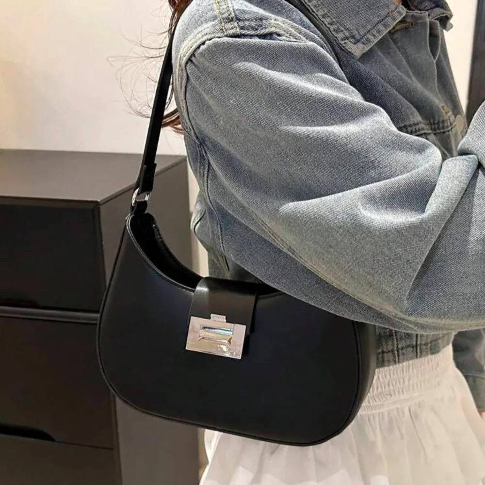 Snygg svart axelväska i skinn med ett stilrent metallspänne framtill. Väskan har en enkel och elegant design, perfekt för att komplettera din outfit. Ej använd . Laukut & Käsilaukut.