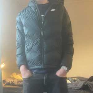 Svart dunjacka från Nike - Säljer en svart dunjacka från Nike med huva och dragkedja. Jackan har en puffig design och är perfekt för kyligare väder. Ny pris 1000