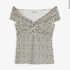 Prickig offshoulder-topp - Snygg offshoulder-topp med svartvitt prickigt mönster. Toppen har en elegant twistdetalj framtill och är perfekt för en trendig look.