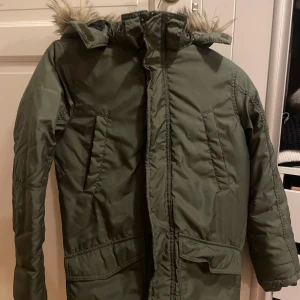 Grön parkajacka från H&M - Säljer en grön parkajacka från H&M med fuskpäls på huvan. Jackan har dragkedja och knappar framtill samt flera praktiska fickor. Perfekt för kyligare dagar. Jackan är väldigt sparsamt använd! Perfekt nu till vintern🥶 jackan är i storlek: 11-12år (152)skriv om ni har frågor!