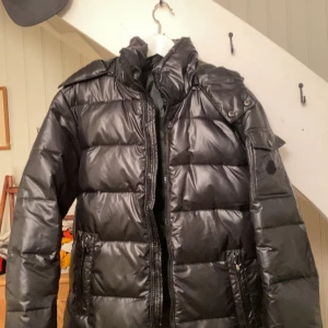 Svart pufferjacka med dragkedja - Snygg svart pufferjacka med dragkedja och hög krage. Jackan har långa ärmar och praktiska fickor framtill. Den är varm och skön. Men om du är sugen att köpa är de ba att höra av sig! 