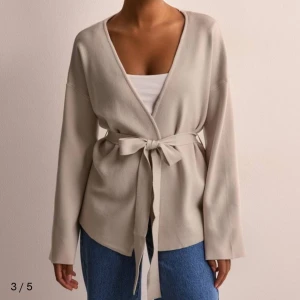 Beige kofta från Object Collectors Item - Snygg beige kofta med lång ärm och knytband i midjan från Object Collectors Item. Perfekt för en stilren och avslappnad look. Passar bra till jeans eller klänning. 