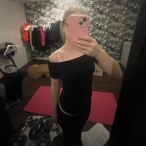 Svart offshoulder topp - Säljer en stilren svart offshoulder topp. Perfekt för en trendig look med sin tighta passform. Toppen är ärmlös och passar bra till både jeans och kjol.