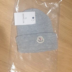 Grå mössa från Moncler - Komm med bud!! Tänk på att org pris är 2000 kr!! Jag har dessvärre inte äkthets bevis men jag tror den är äkta. Den är helt ny och har inga defekter! Kontakta mig vid minsta funderingar!