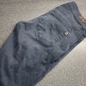 Svarta byxor Dondup  - Snygga grå/blå byxor från Dondup med klassisk design. Byxorna har en rak passform och är perfekta för en stilren look. De har fem fickor och en knappgylf.