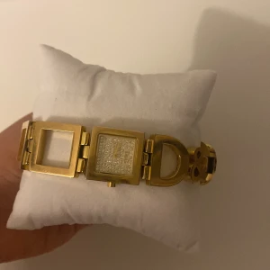 Guldklocka från D&G - En fin guldklocka från Dolce & gabbane med fyrkantiga länkar och en glittrig detalj i mitten. Lite större armband men det går att fixa ganska enkelt.