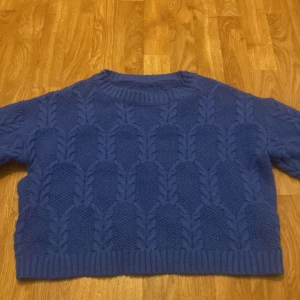 Blå stickad tröja - Säljer en mysig blå stickad tröja med ett snyggt flätmönster. Tröjan har långa ärmar och en rund halsringning. Perfekt för kyliga dagar!