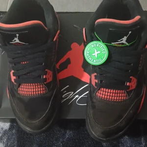 Air Jordan 4 Retro (GS) - Säljer ett par Air Jordan 4 Retro i svart och röd färg. Skorna har den klassiska Jumpman-loggan och snörning. Perfekt för sneakerheads som vill ha en ikonisk stil.