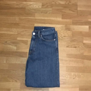 Blå jeansbyxor - Säljer ett par klassiska blå jeansbyxor med normal passform. De har en midwaist design och är perfekta för en avslappnad stil. Byxorna har en dragkedja och knapp framtill.