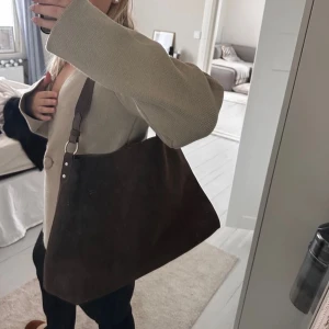 Brun axelväska från Bik Bok - Snygg brun axelväska från Bik Bok i syntetmaterial. Väskan har en enkel design med en bred axelrem och stängs med en knapp. Perfekt för att bära dina dagliga nödvändigheter med stil.