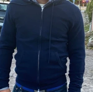 Blå huvtröja med dragkedja - Säljer en stilren blå huvtröja med dragkedja. Perfekt för en avslappnad look. Tröjan har långa ärmar och en justerbar huva. Äkta khamir från Johan finns kvitto 