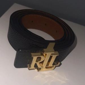 Svart bälte med guldspänne - Snyggt svart bälte från Ralph Lauren med ett iögonfallande guldspänne. Perfekt för att ge en stilren touch till din outfit. Tillverkat i skinn för en lyxig känsla.