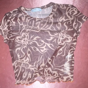 Mesh topp med tribal mönster - Snygg och trendig mesh topp från bershka med tribal mönster i beige och brun. Toppen är kortärmad och har en croppad passform med vågig kant nedtill. Perfekt för en edgy look!