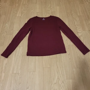 Vinröd långärmad tröja från H&M - Säljer en vinröd långärmad tröja från H&M i ekologisk bomull. Perfekt för en avslappnad stil och enkel att matcha med andra plagg. Tröjan är en del av H&M:s Basic-kollektion.