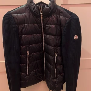Svart dunjacka från Moncler - Snygg mörkblå cardigan från Moncler med stickade ärmar och dragkedja framtill. Jackan har två praktiska fickor med dragkedjor och Moncler-logga på ärmen, säljer pågrund av att den inte kommer till användning och det längre inte är min stil, använt den bara en säsong vid kanske 5 tillfälllen, jackan är köpt på mytheresa och är äkta, jackan är i sl xs/S passar som två storlekar.