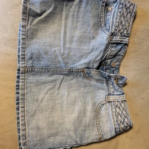 Jeanskjol från Vila - Snygg jeanskjol från Vila i en klassisk blå färg. Kjolen har flätade detaljer vid fickorna och midjan som ger en unik touch. Perfekt för en avslappnad stil.