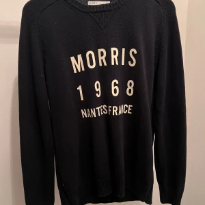 Svart tröja från Morris - Säljer en svart tröja från Morris med texten 'Morris 1968 Nantes France' tryckt på framsidan. Tröjan har långa ärmar och en rund halsringning. Perfekt för en stilren och avslappnad look.
