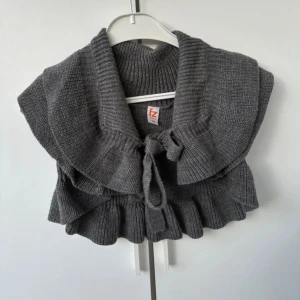 Grå bolero - Säljer en superfin grå stickad bolerotopp med volangdetaljer och knytband framtill. Perfekt att ha över en blus eller klänning för en extra touch. Den är i mycket bra skick och passar perfekt för höst och vår. Storleken är dam S.