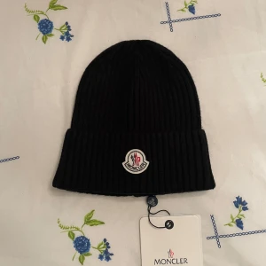 Svart ribbad mössa från Moncler - Snygg svart ribbad mössa från Moncler med broderad logotyp framtill. Perfekt för att hålla värmen under kyliga dagar.