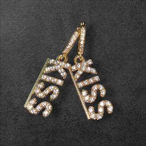 Snygga örhängen i guld med glittrande stenar som bildar ordet 'KISS'. Perfekta för att ge en extra touch till din outfit. De hängande bokstäverna ger en lekfull och trendig look.