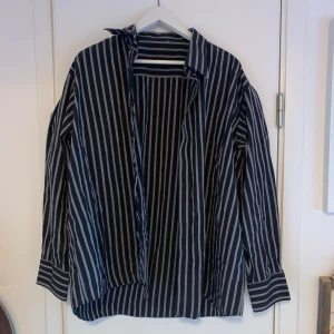 Svartvit randig skjorta - Snygg svartvit randig skjorta med långa ärmar och klassisk krage. Perfekt för en stilren look. Skjortan har en avslappnad passform och är tillverkad i ett lätt material.