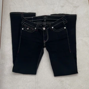 Svarta jeans från True Religion - Snygga svarta jeans från True Religion med låg midja och flare-stil. De har vita och röda kontrastsömmar.