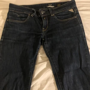 Mörkblå jeans från Replay - Snygga mörkblå jeans från Replay, lågmidjade. Bootcut, femficksdesign och knappgylf. Perfekta för en avslappnad stil. Märkesdetaljer syns på baksidan och insidan av midjan. 