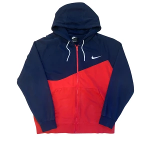 Blå och röd hoodie från Nike - Säljer en snygg blå och röd hoodie från Nike i storlek XL med dragkedja och huva. Den har en stor vit Nike-logga på ryggen och en midre på bröstet. Mycket bra skick. 