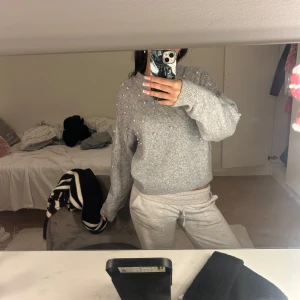 Grå tröja med pärlor från H&M - Säljer en mysig grå tröja från H&M dekorerad med pärlor. Tröjan har en normal passform och långa ärmar, perfekt för kyligare dagar. Den är tillverkad i ett mjukt material som ger en bekväm känsla. Perfekt för att lägga till lite stil i vardagslooken.