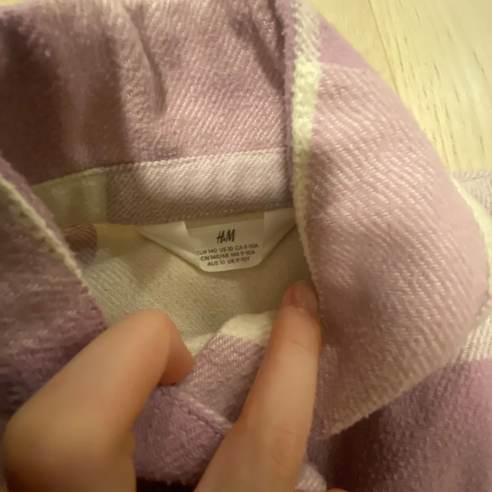 Säljer en snygg rutig jacka från H&M i lila och vit. Skjortan har långa ärmar och knappar framtill. Perfekt för en avslappnad stil.. Takit.