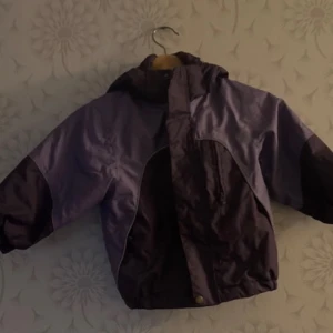 Lila regnjacka med matchande byxor - Säljer en lila regnjacka med huva och matchande byxor. Jackan har långa ärmar och reflexdetaljer för extra synlighet. Perfekt för regniga dagar!