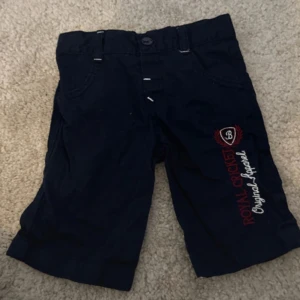 Svarta shorts från Royal Closet - Snygga svarta shorts från Royal Closet med broderad logga på sidan. De har knappar och bälteshällor för en justerbar passform. Perfekta för en avslappnad stil.