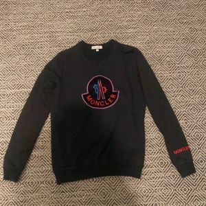 Svart tröja från Moncler - Äkta Snygg svart tröja från Moncler storlek s med deras ikoniska logga broderad i rött och blått på framsidan. Tröjan har långa ärmar och Moncler-text på ärmen. Perfekt för en stilren look.  Skick otroligt bra använd 2 gånger pris 1200 kan diskuteras vid snabb affär 