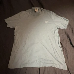 Ljusblå t-shirt från Adidas - Säljer en ljusblå t-shirt från Adidas med det klassiska logotypen broderad på bröstet. Perfekt för en avslappnad stil. T-shirten är kortärmad och tillverkad i mjukt material. L: 69, B: 42