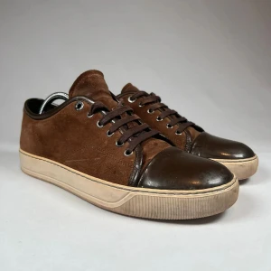 Bruna lanvin captoes  - Snygga bruna lanvins med en kombination av mocka och skinn. Skorna har en klassisk snörning och en ljus sula som ger en fin kontrast. Perfekta för en stilren look.