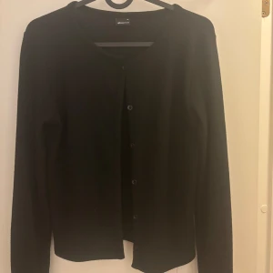 Svart kofta från Gina - Snygg svart kofta från Gina tricot med knappar framtill. Perfekt för våren när vädret håller på att bli bättre. Ganska tunt material men liten i storleken. Jag brukar ha storlek s men det blev M istället och det funkar jätte bra. Som man ser på bilden är den knappt använd. Säljer för 200 kr men priset kan diskuteras då den kostat ordinarie 300 kr.
