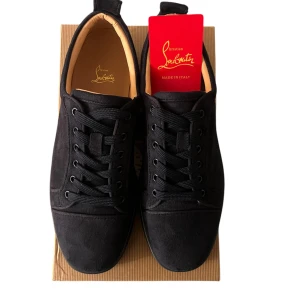 Navy blå sneakers från Christian Louboutin - Snygga navy-blå sneakers från Christian Louboutin med den ikoniska röda sulan. Skorna har en stilren design med snörning och är tillverkade i ett elegant material. Perfekta för den som vill ha en touch av lyx i vardagen.