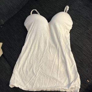 Vit ärmlös linnetopp - Säljer en stilren vit linnetopp med smala axelband. Toppen är ärmlös och har en enkel design som passar perfekt till sommaren. Perfekt för en avslappnad look. Den har en inbyggd bh, men vet inte riktigt storleken, den är under 75 c vet jag. 