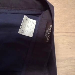 Svarta kostymbyxor från Rose & Born - Eleganta svarta kostymbyxor från Rose & Born, tillverkade i Italien. Byxorna har en klassisk rak passform och är perfekta för en stilren look. De är gjorda i ett fint material som ger en lyxig känsla. Notera storlek 44