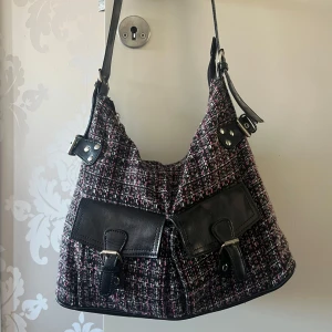 Rutig axelväska  - Snygg rutig axelväska med svarta skinnremmar och detaljer. Köpt på plick. Lite sliten i bandet men för övrigt i fint skick. 